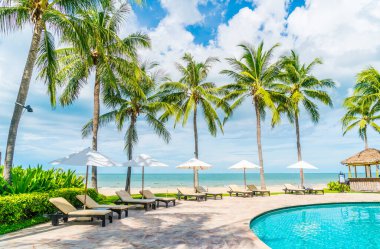 Güzel tropikal plaj ve deniz şemsiyesi ve sandalyesi otel tatil ve tatil için yüzme havuzunda.