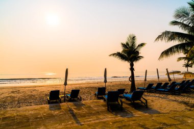 Güneş doğarken palmiye ağacı ve deniz plajı olan şemsiye koltuğu plajı - tatil ve tatil konsepti
