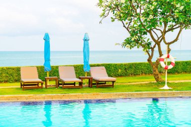 Sandalye havuzu ve şemsiyeyle okyanus arka planında yüzme havuzu