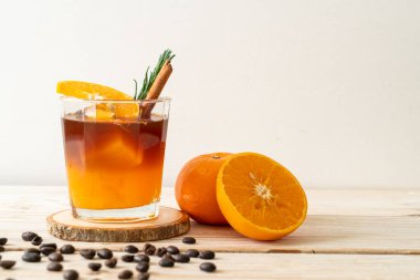 Bir bardak buzlu americano sade kahve ve ahşap arka planda biberiye ve tarçınla süslenmiş portakal ve limon suyu.