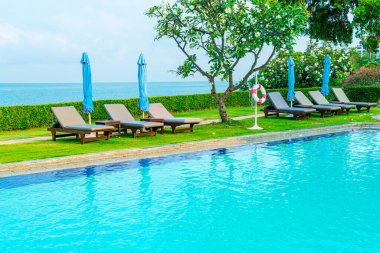 Sandalye havuzu ve şemsiyeyle okyanus arka planında yüzme havuzu