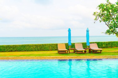 Sandalye havuzu ve şemsiyeyle okyanus arka planında yüzme havuzu