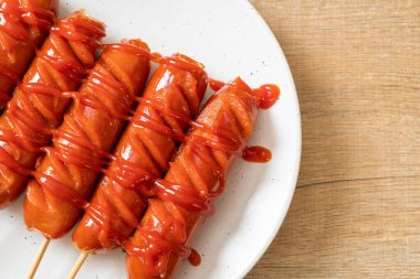 Beyaz tabakta ketçaplı kızarmış sosis şişi.