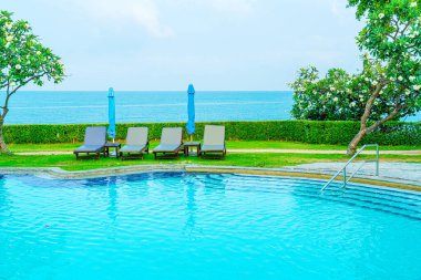 Sandalye havuzu ve şemsiyeyle okyanus arka planında yüzme havuzu