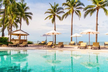 Güzel tropikal plaj ve deniz şemsiyesi ve sandalyesi otel tatil ve tatil için yüzme havuzunda.