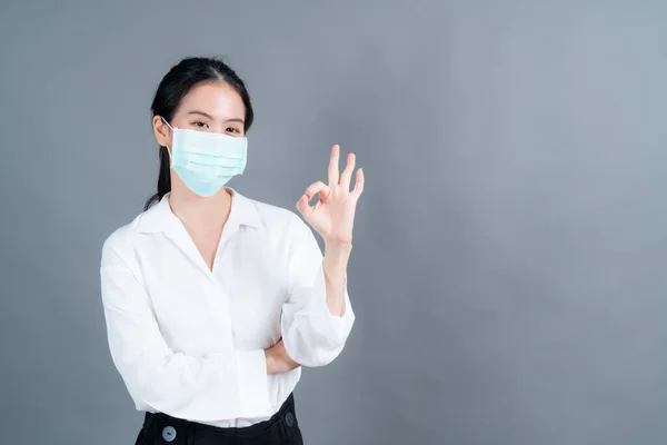 Young Asian woman wearing medical face mask protects filter dust pm2.5 anti-pollution, anti-smog, COVID-19 and showing OK sign