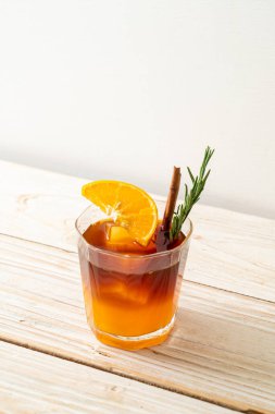 Bir bardak buzlu americano sade kahve ve ahşap arka planda biberiye ve tarçınla süslenmiş portakal ve limon suyu.