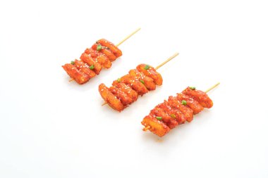 Kızarmış Kore pirinç keki (Tteokbokki) beyaz arka planda izole edilmiş baharatlı sosla şişlenmiş.