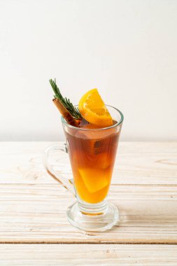 Bir bardak buzlu americano sade kahve ve ahşap arka planda biberiye ve tarçınla süslenmiş portakal ve limon suyu.