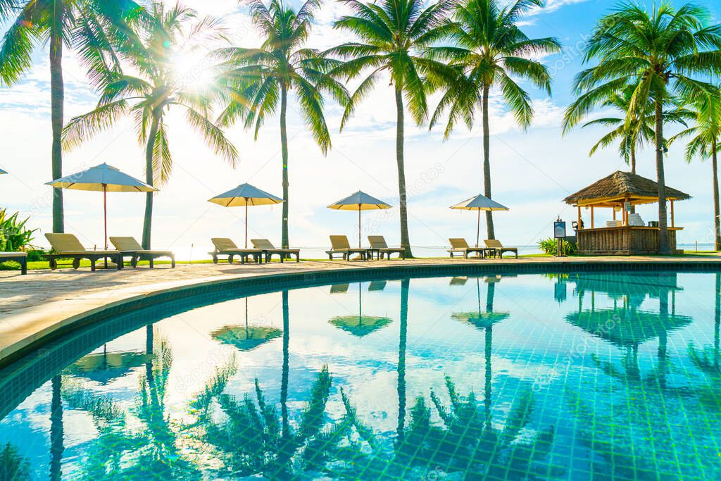 Beautiful luxury umbrella and chair around outdoor swimming pool in hotel and resort with coconut palm tree on blue sky - vacation and holiday concept