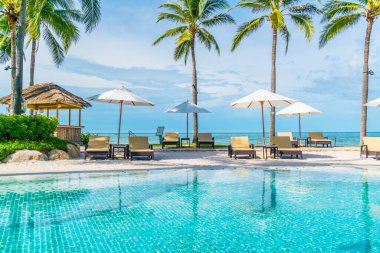 Güzel tropikal plaj ve deniz şemsiyesi ve sandalyesi otel tatil ve tatil için yüzme havuzunda.