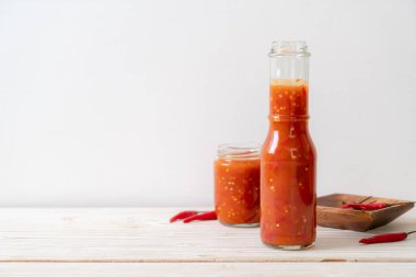 Şişede kırmızı biber ya da kırmızı biber sosu ve arka planda kavanoz.