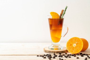 Bir bardak buzlu americano sade kahve ve ahşap arka planda biberiye ve tarçınla süslenmiş portakal ve limon suyu.