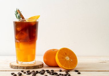 Bir bardak buzlu americano sade kahve ve ahşap arka planda biberiye ve tarçınla süslenmiş portakal ve limon suyu.