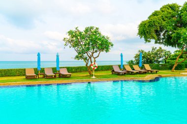 Sandalye havuzu ve şemsiyeyle okyanus arka planında yüzme havuzu