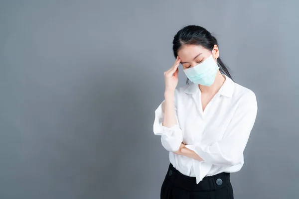 Asian woman wearing medical face mask protects filter dust pm2.5 anti-pollution, anti-smog, and COVID-19 and have headache on grey background