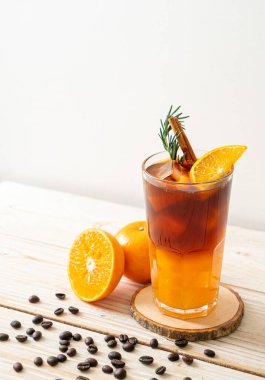 Bir bardak buzlu americano sade kahve ve ahşap arka planda biberiye ve tarçınla süslenmiş portakal ve limon suyu.