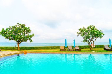 Sandalye havuzu ve şemsiyeyle okyanus arka planında yüzme havuzu