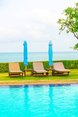 Sandalye havuzu ve şemsiyeyle okyanus arka planında yüzme havuzu