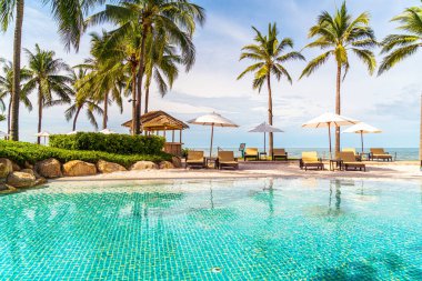 Güzel tropikal plaj ve deniz şemsiyesi ve sandalyesi otel tatil ve tatil için yüzme havuzunda.
