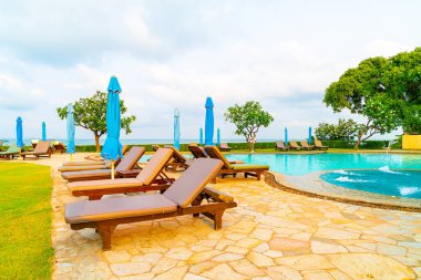 Sandalye havuzu ve şemsiyeyle okyanus arka planında yüzme havuzu