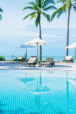 Güzel tropikal plaj ve deniz şemsiyesi ve sandalyesi otel tatil ve tatil için yüzme havuzunda.