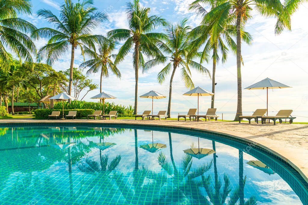 Beautiful luxury umbrella and chair around outdoor swimming pool in hotel and resort with coconut palm tree on sunset  or sunrise sky - holiday and vacation concept