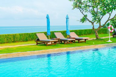 Sandalye havuzu ve şemsiyeyle okyanus arka planında yüzme havuzu