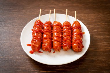 Beyaz tabakta ketçaplı kızarmış sosis şişi.