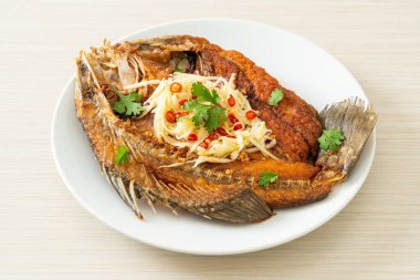 Balık soslu kızarmış deniz levreği balığı ve tabakta baharatlı salata.