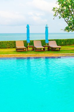 Sandalye havuzu ve şemsiyeyle okyanus arka planında yüzme havuzu