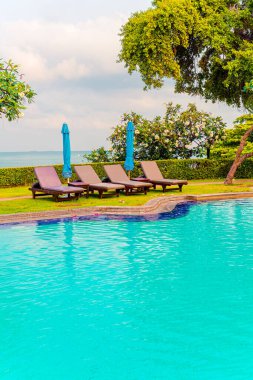 Sandalye havuzu ve şemsiyeyle okyanus arka planında yüzme havuzu