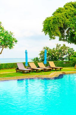 Sandalye havuzu ve şemsiyeyle okyanus arka planında yüzme havuzu