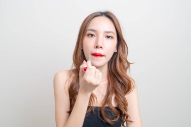 Güzel Asyalı kadın portresi makyaj yapıyor ve beyaz arka planda kırmızı ruj kullanıyor.