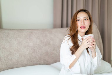 Portre güzel Asyalı kadın uyanır ve elinde kahve fincanı ya da kupayla sabah uyanır.