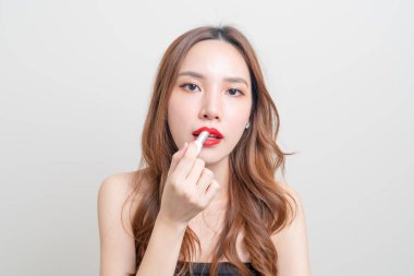 Güzel Asyalı kadın portresi makyaj yapıyor ve beyaz arka planda kırmızı ruj kullanıyor.