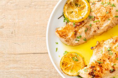 Beyaz tabakta tereyağlı ızgara tavuk, limon ve sarımsak.