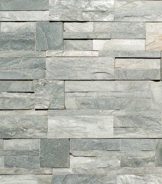 Doğal dokusu ve ince renk varyasyonları olan dikdörtgen gri fayanslardan yapılmış dekoratif taş bir duvara yakın çekim. Mimari, tasarım ve arkaplan kullanımı için uygun pürüzlü yüzey ve modern duvarcılık deseni.
