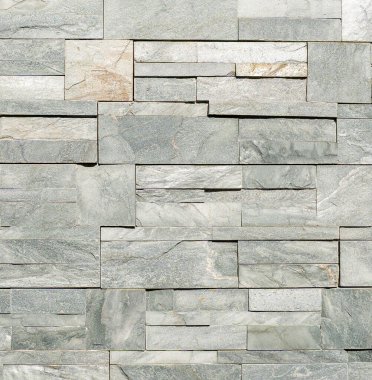 Doğal dokusu ve ince renk varyasyonları olan dikdörtgen gri fayanslardan yapılmış dekoratif taş bir duvara yakın çekim. Mimari, tasarım ve arkaplan kullanımı için uygun pürüzlü yüzey ve modern duvarcılık deseni.