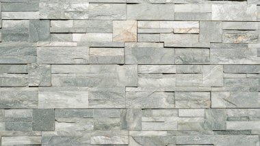 Doğal dokusu ve ince renk varyasyonları olan dikdörtgen gri fayanslardan yapılmış dekoratif taş bir duvara yakın çekim. Mimari, tasarım ve arkaplan kullanımı için uygun pürüzlü yüzey ve modern duvarcılık deseni.