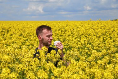 Kolza tarlasında polene alerjisi olan bir adam burnunu kapatır..