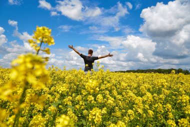 Kolza tohumu tarlasında elleri havada mutlu bir çiftçi duruyor..