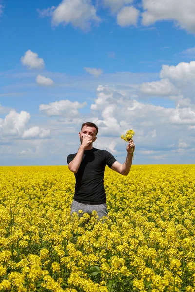 菜の花畑で花粉症の男が鼻を閉じて — ストック写真