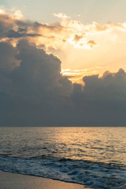 Denizin üzerinde şafak, bulutların ardında güneş yükseliyor.