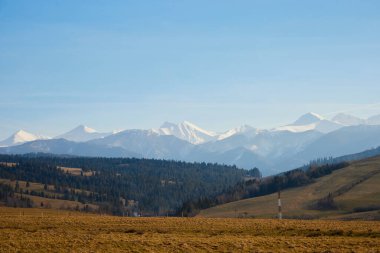 Güneşli dağ manzarası, ilkbahar çayırı ve ufuktaki dağ zirveleri