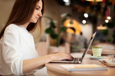 Her gün dizüstü bilgisayarda yazan ve kafede kahve molası veren genç bir kadın. Kadın yönetici proje için bilgi düzenliyor ve kahve dükkanında otururken notlar alıyor.