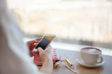 Süslü pembe günlük ve altın kalemle kahve molası sırasında kahve içerken cep telefonu kullanan kadın eller. Uzayı kopyala Zaman yönetimi ve çoklu görev kavramı.