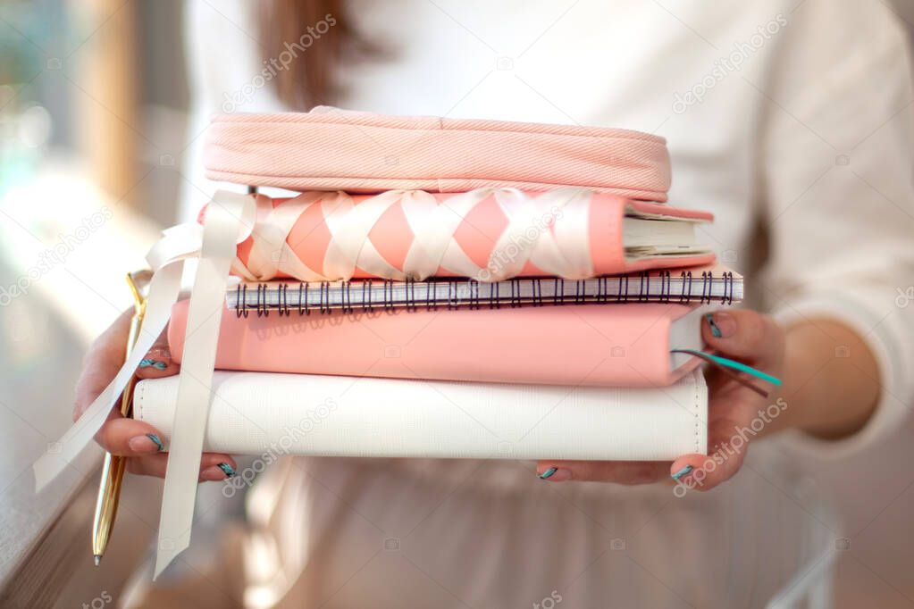 Woman hands carrying stylish designed coral and white coloured stack of diaries with gold pen. Organiser and planner addicted people. Choosing and sorting journals.