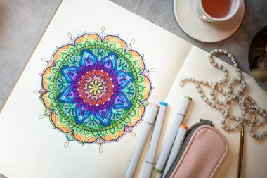 Renkli mandala sanat kitabının üst görüntüsü renkli kalemler, pembe kalem kutusu ve tespih boncukları. Meditasyon tekniği olarak renkli mandalalar kavramı.
