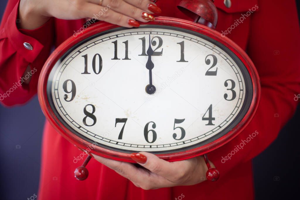 Woman in red dress holding with hands a huge clock showing 12 midnight. Merry Christmas & New Year's Eve concept. Festive holidays celebration. Copy space.